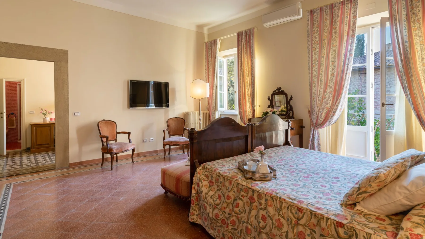 A bedroom with a patterned bedspread, television, and tall windows.