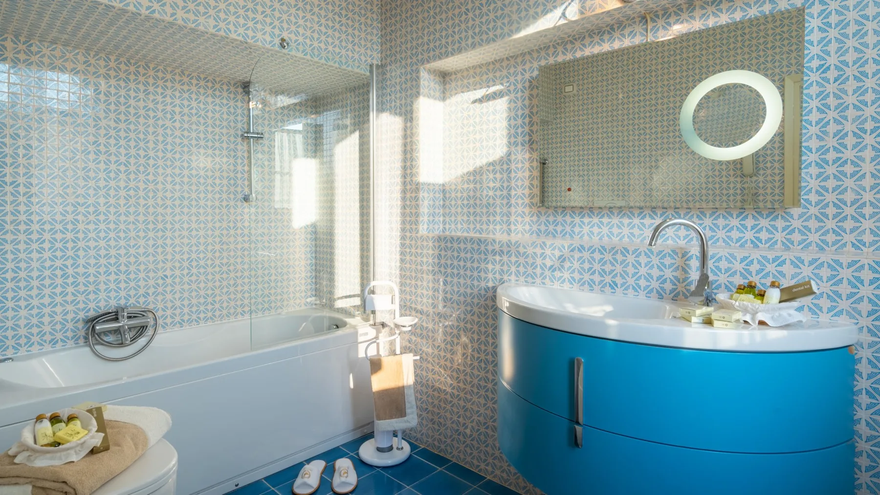 A tiled bathroom with a bathtub, blue vanity, and round mirror.
