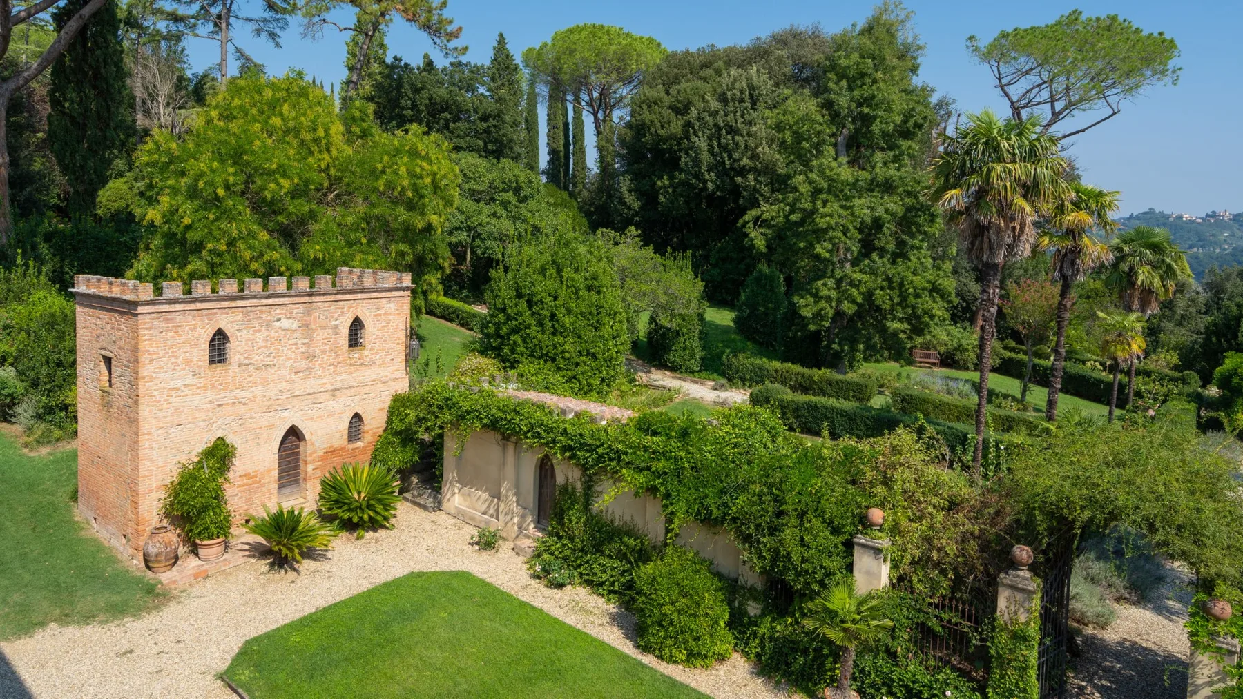 A brick garden building stands beside a gravel path amid lush greenery.