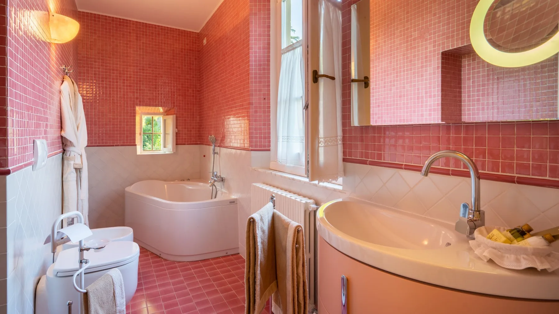 A bathroom with pink tiled walls and a bathtub beneath the window.