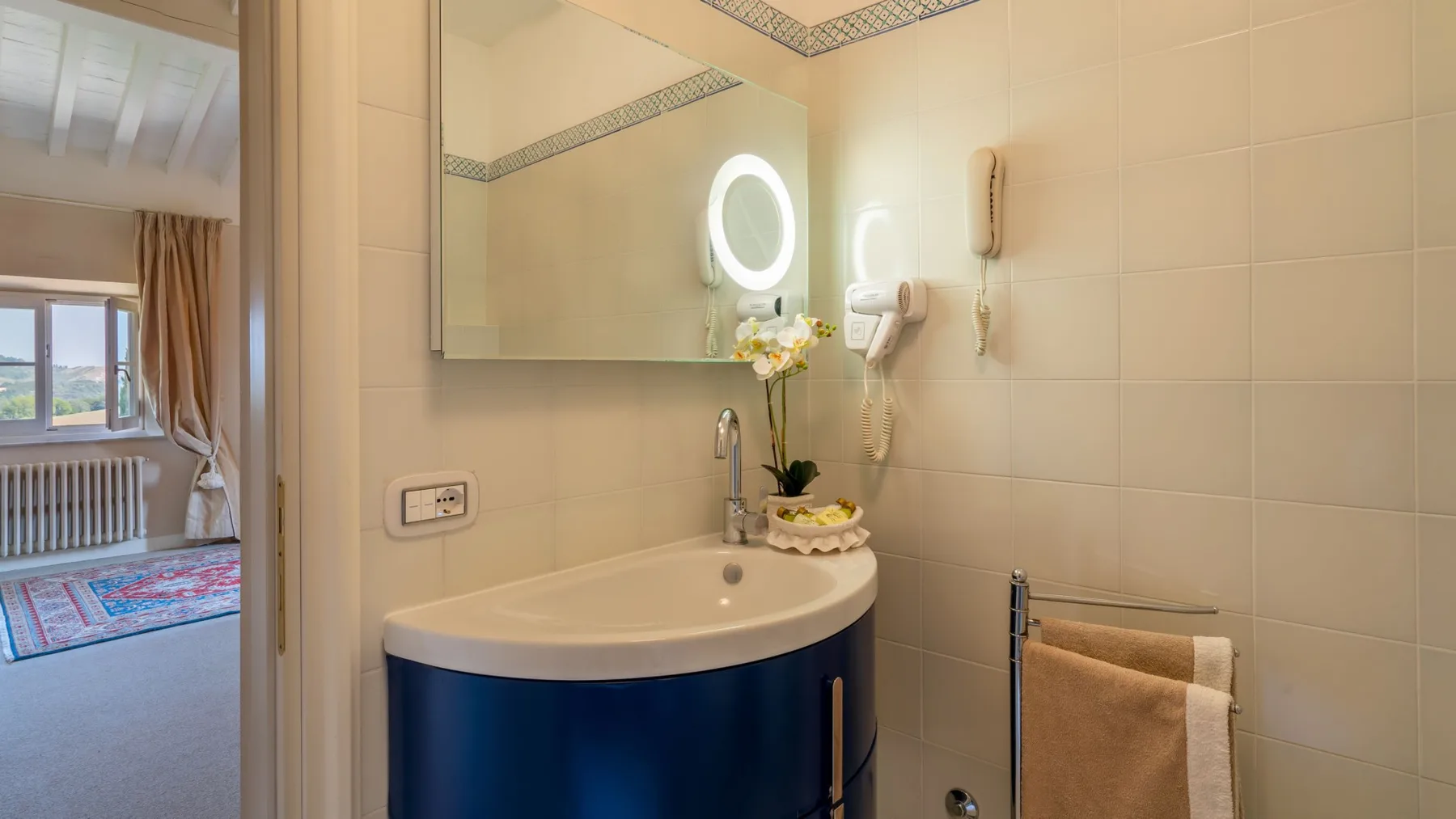A bathroom with a curved vanity, illuminated mirror, and towel rail.
