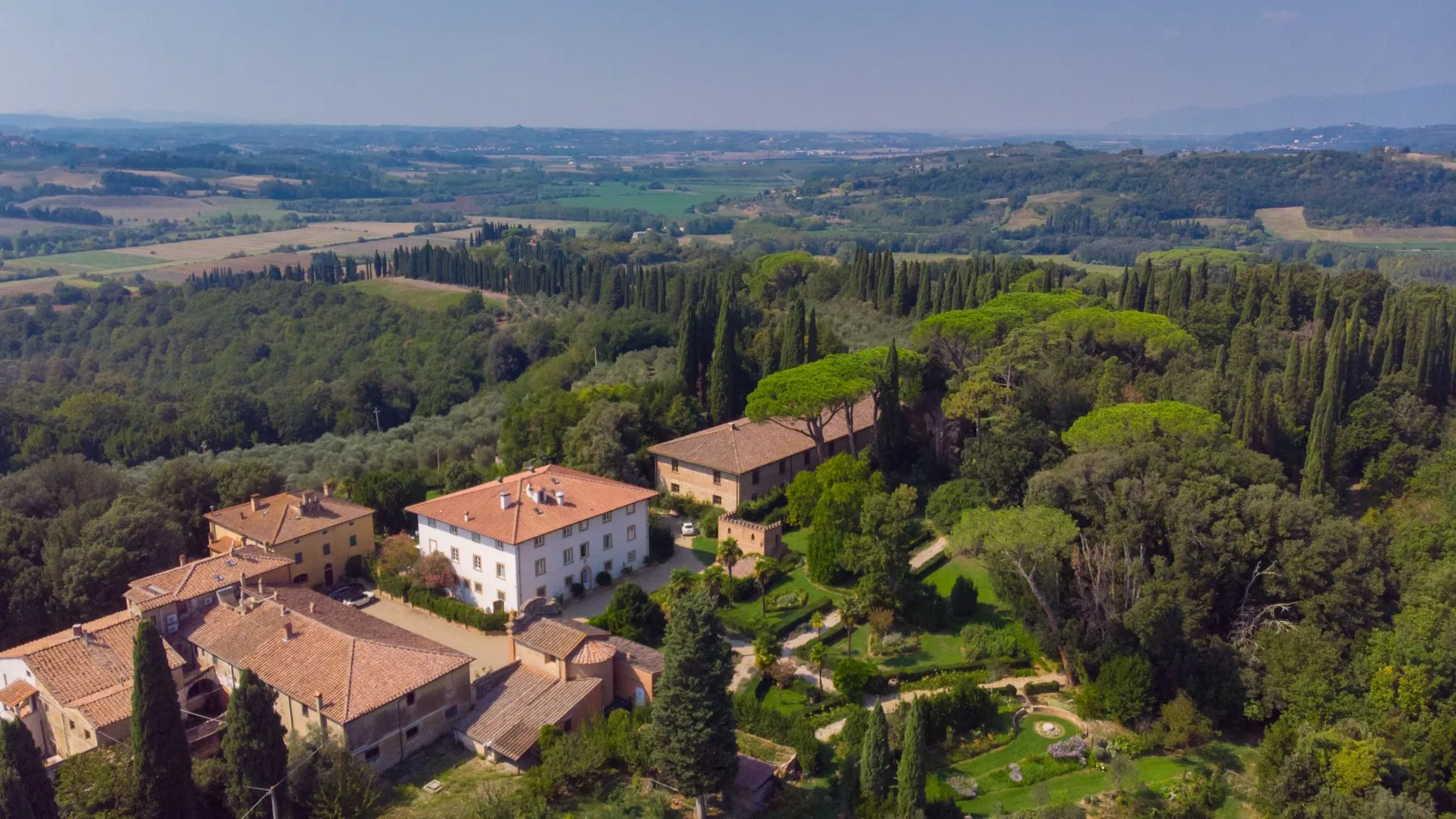 An aerial view of a countryside estate surrounded by wooded hills and fields.