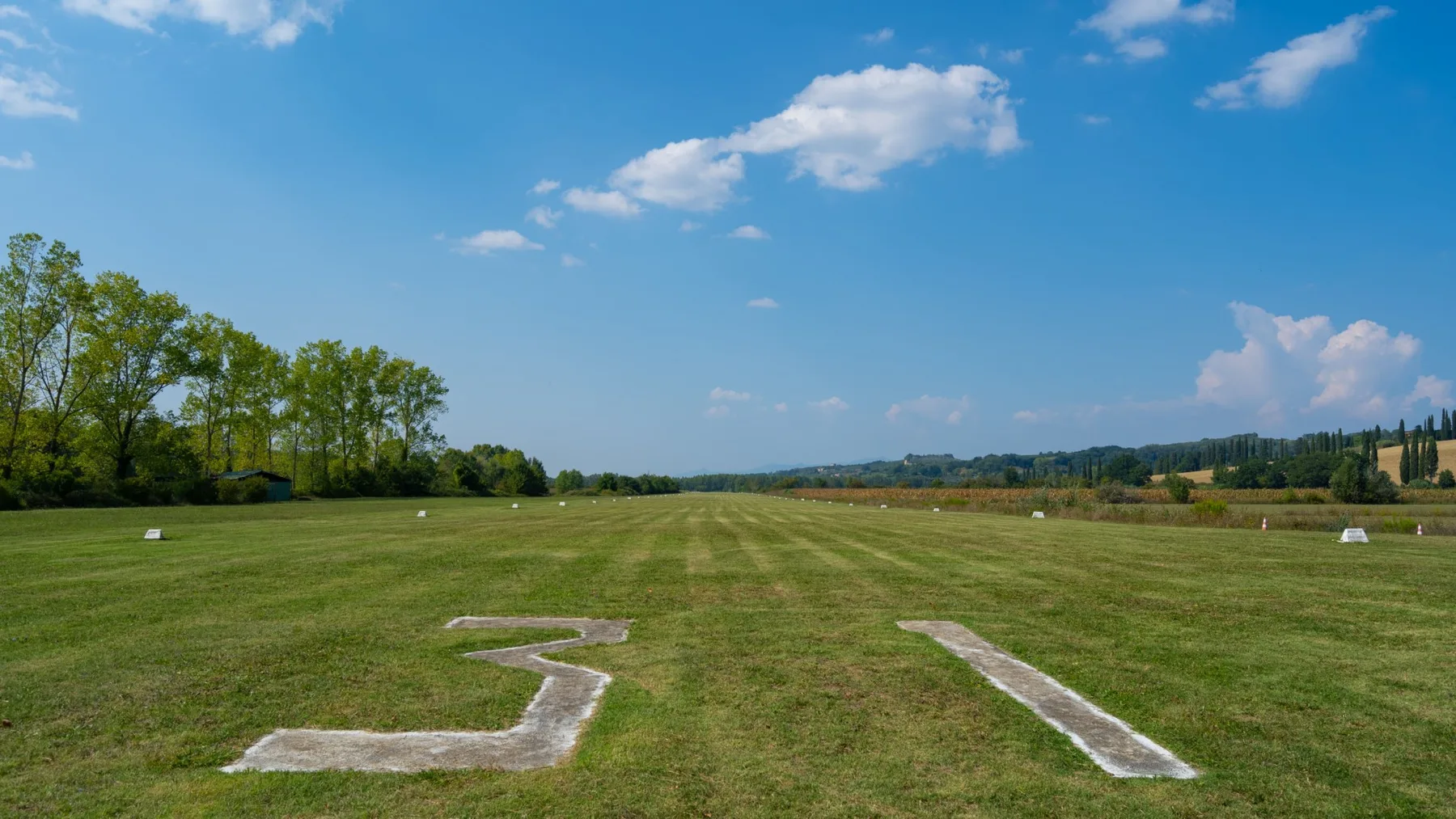 An open grassy field stretches beneath a blue sky, with white field markings in front.