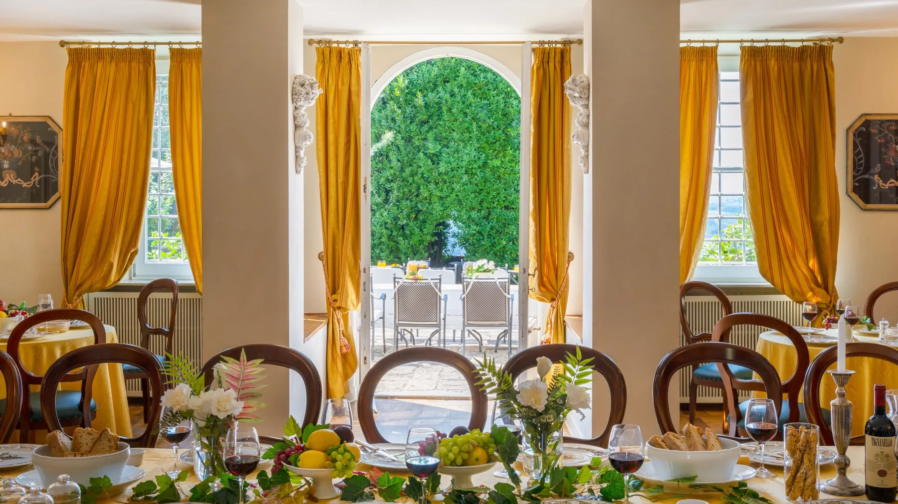 A dining room with a set table in front of an arched opening to a leafy garden.