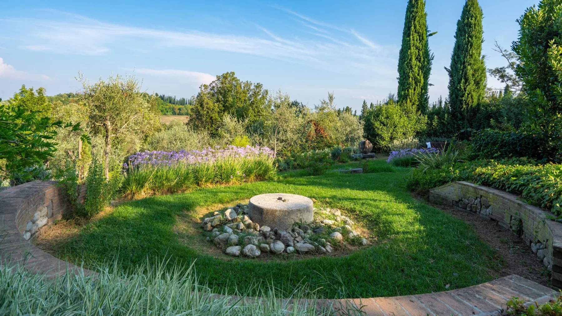 A landscaped garden with a circular stone feature and surrounding greenery.