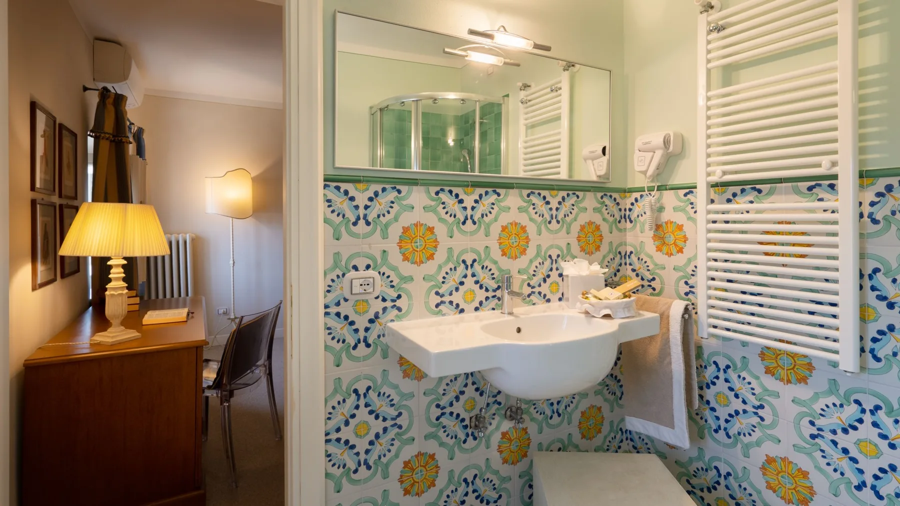 A tiled bathroom with a sink, mirror, and wall-mounted towel warmer.