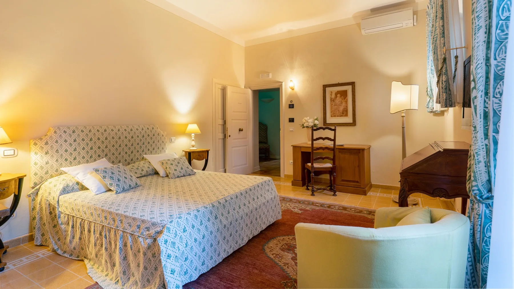 A bedroom with a patterned bedspread and a wooden desk beside the open doorway.