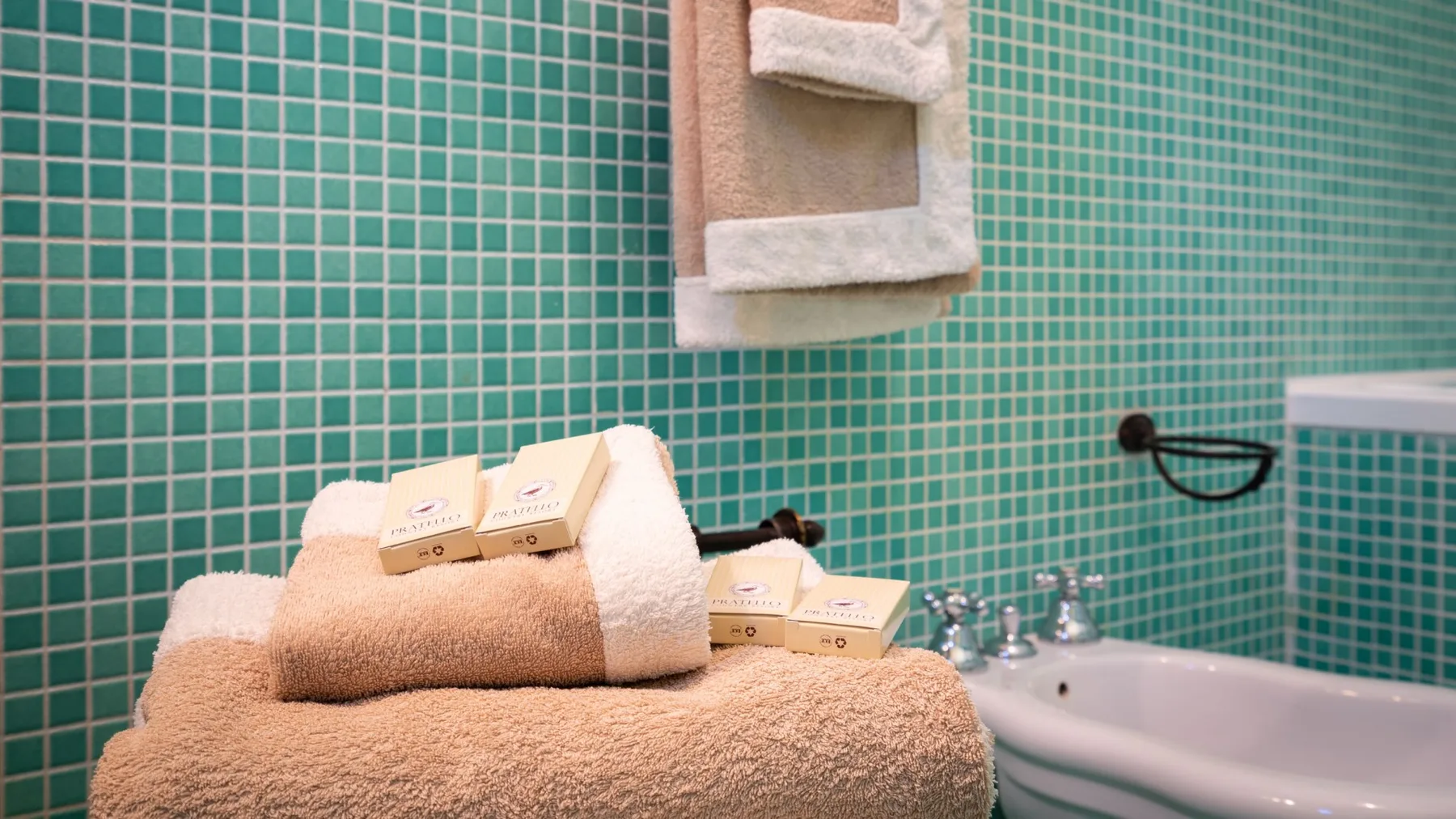A tiled bathroom with folded towels and toiletries beside a sink.