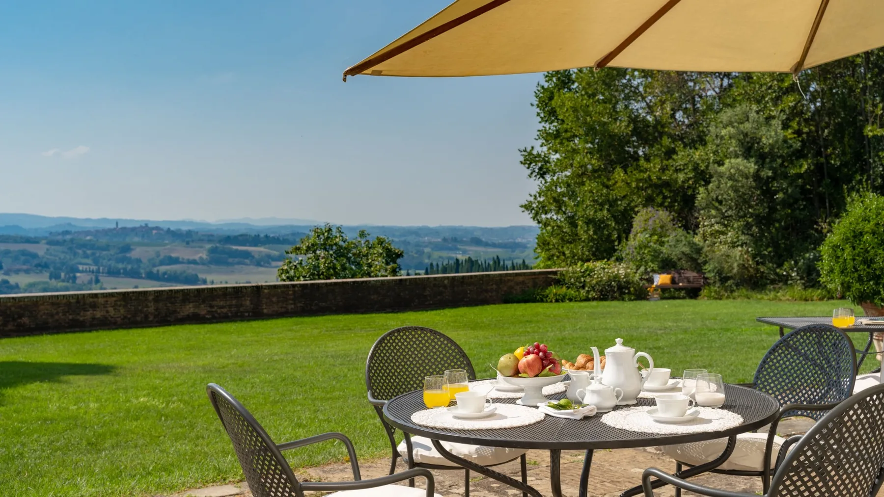 An outdoor dining area with a table and chairs on a lawn overlooking the countryside.