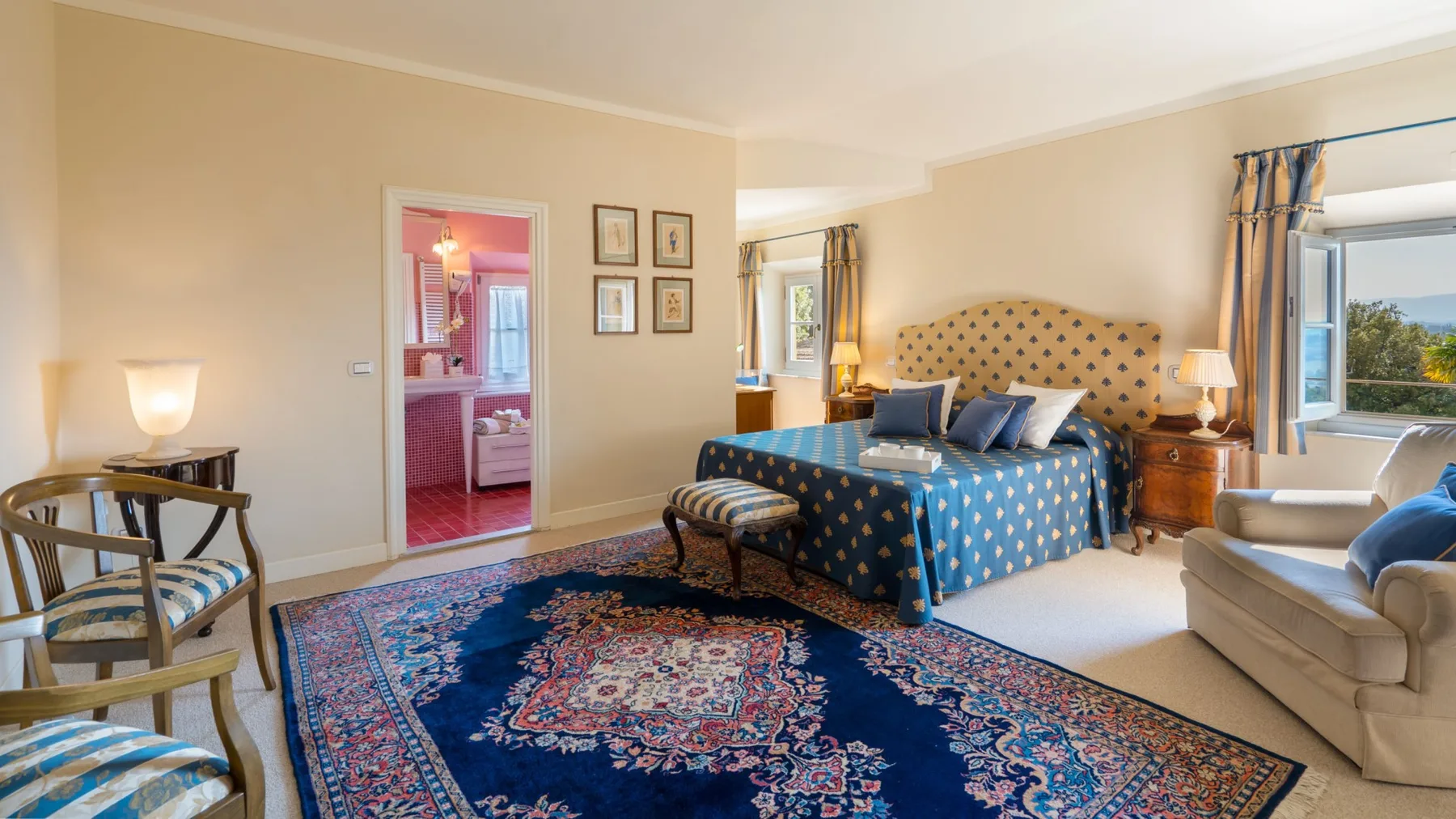 A bedroom with a blue patterned bed, a large rug, and seating.