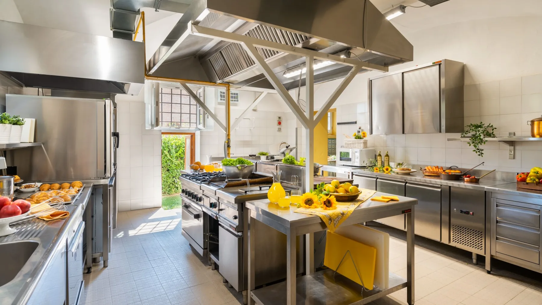 A commercial kitchen with stainless-steel worktables, cooking equipment, and overhead ventilation.