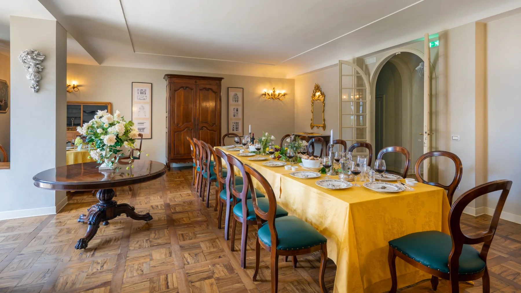 A formal dining room with a long table set with dishes and flowers.