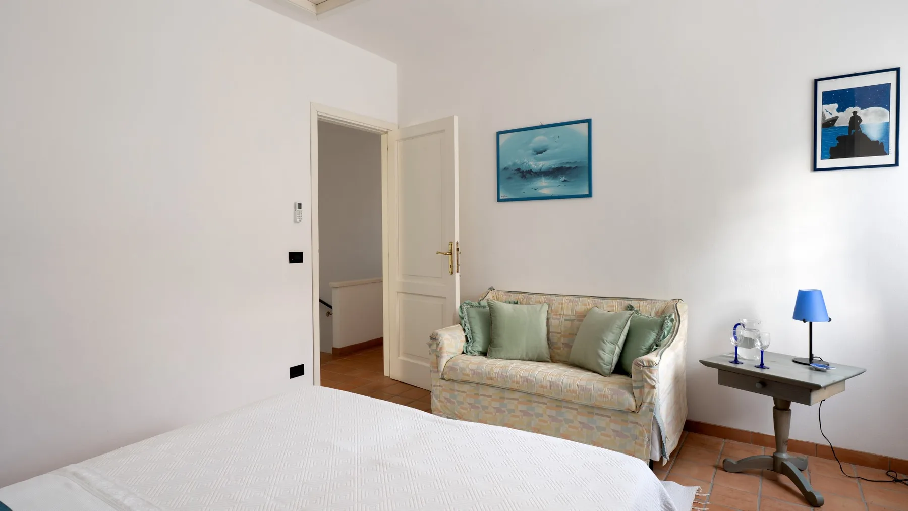 A bright bedroom with a bed, a small sofa, and a bedside table.