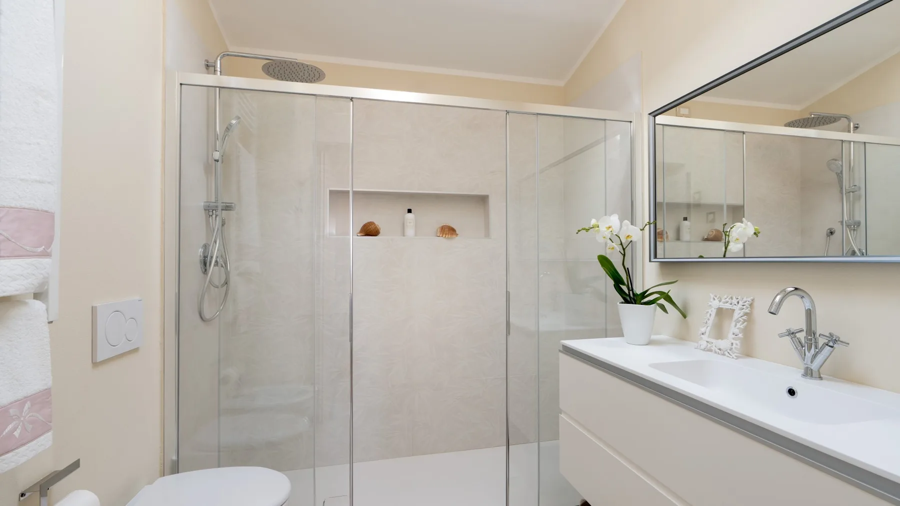 A bathroom with a glass shower and a long vanity topped by a sink.