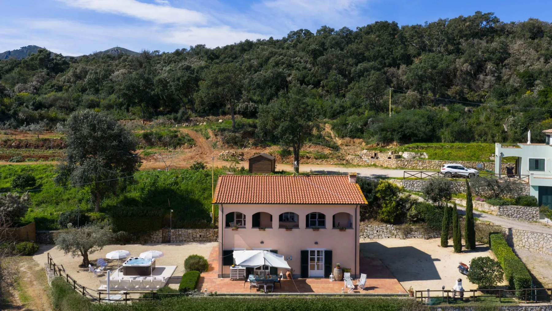 A two-story building with a tiled roof stands beside a wooded hillside.