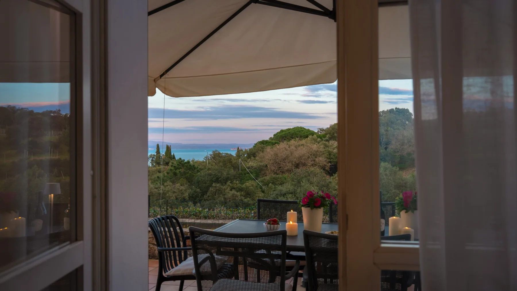 A covered outdoor dining area overlooks green trees and the sea.