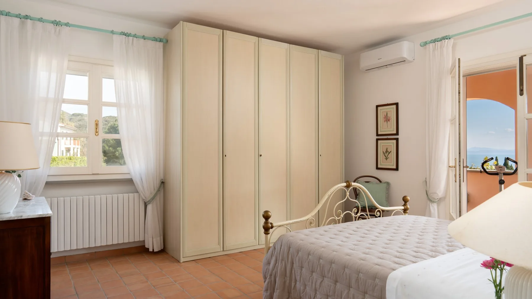 A bedroom with a large wardrobe, a bed, and windows overlooking the sea.