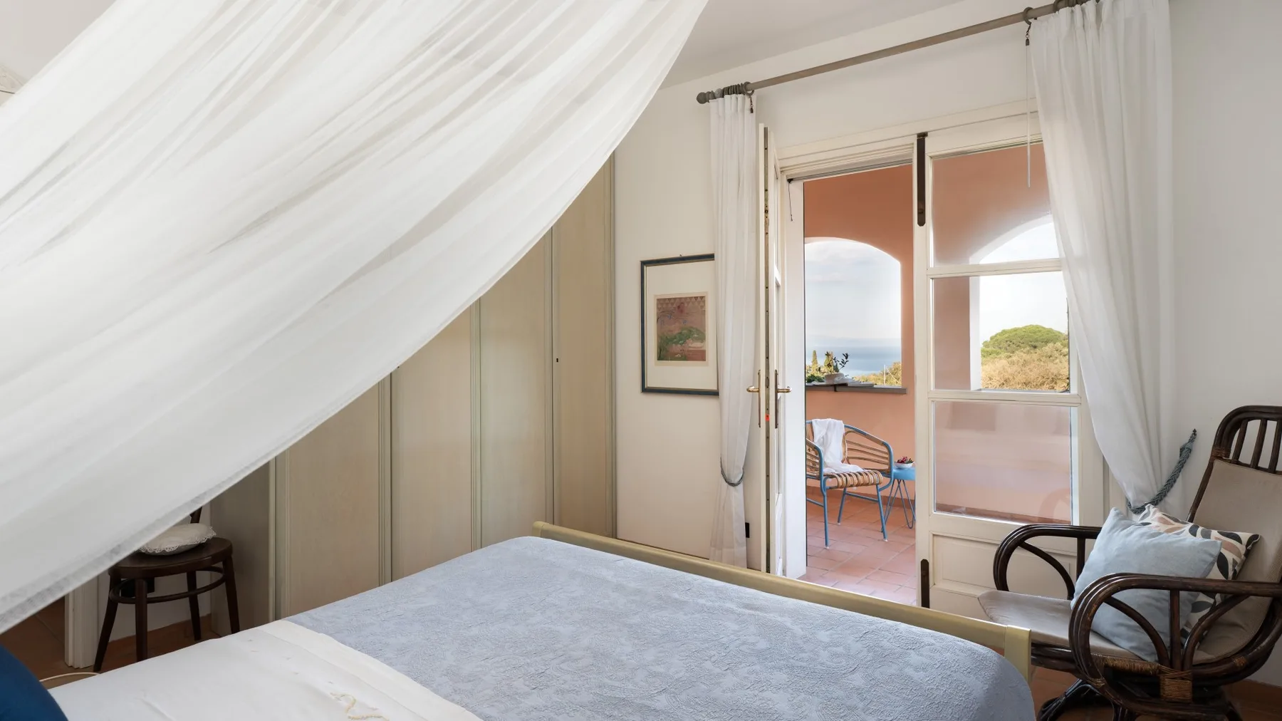 A bedroom with a bed beneath a white canopy and glass doors opening to a balcony.