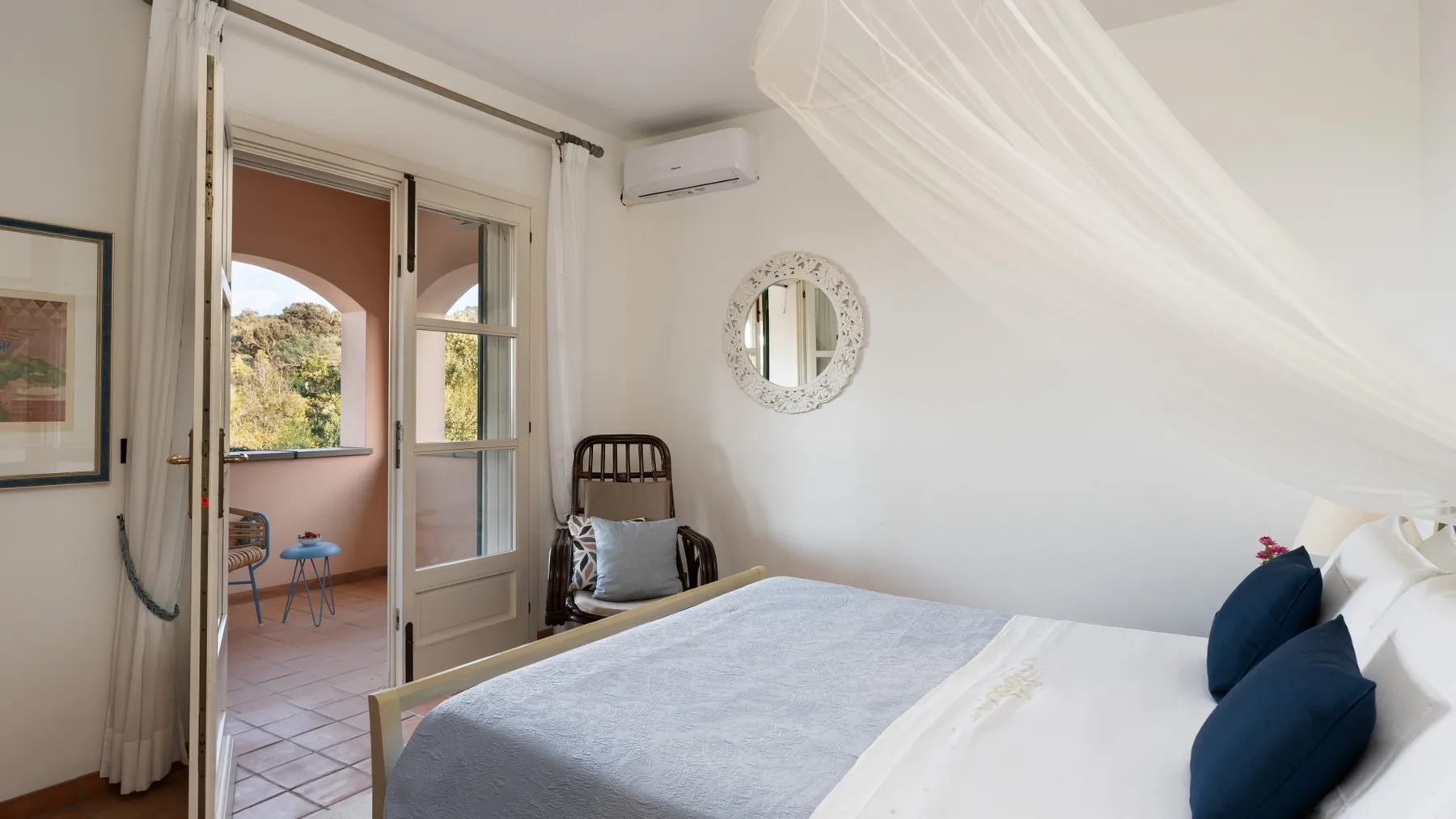 A bright bedroom with a bed, sheer canopy, and an open doorway.