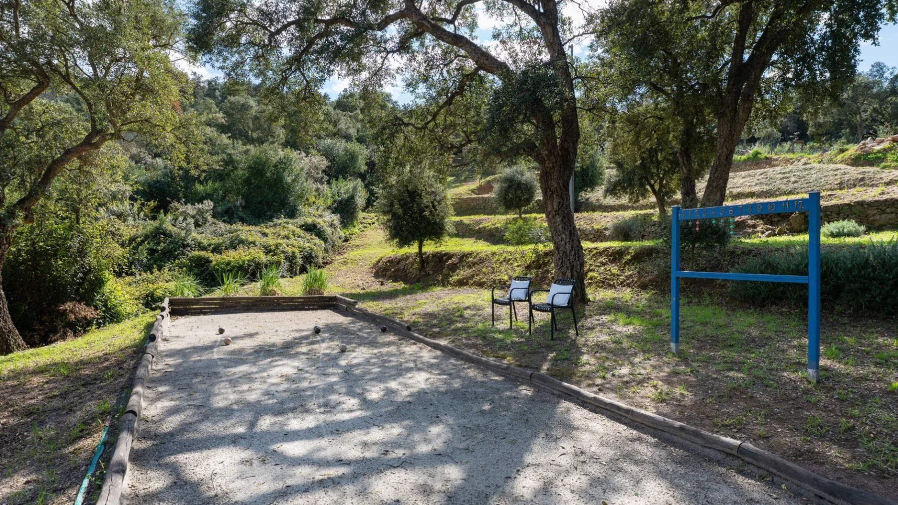 A gravel playing area sits beneath trees beside a blue outdoor frame.
