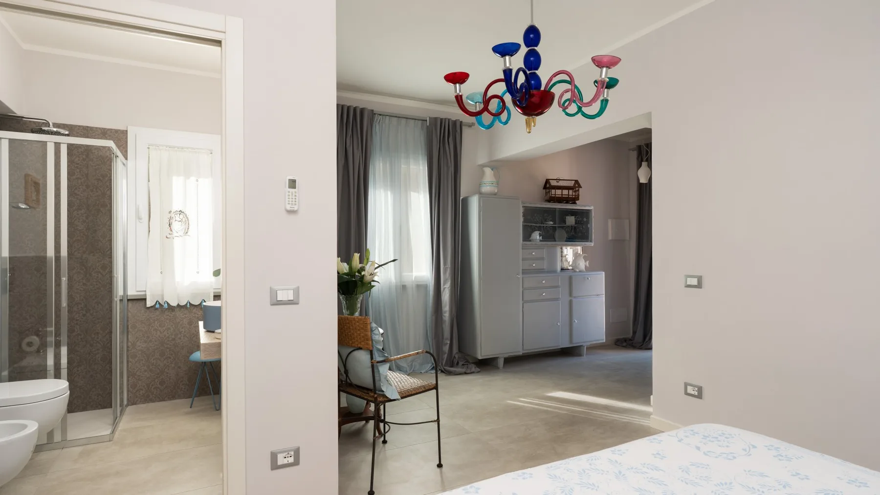 A bright living area with a colorful chandelier and a glass-front cabinet.