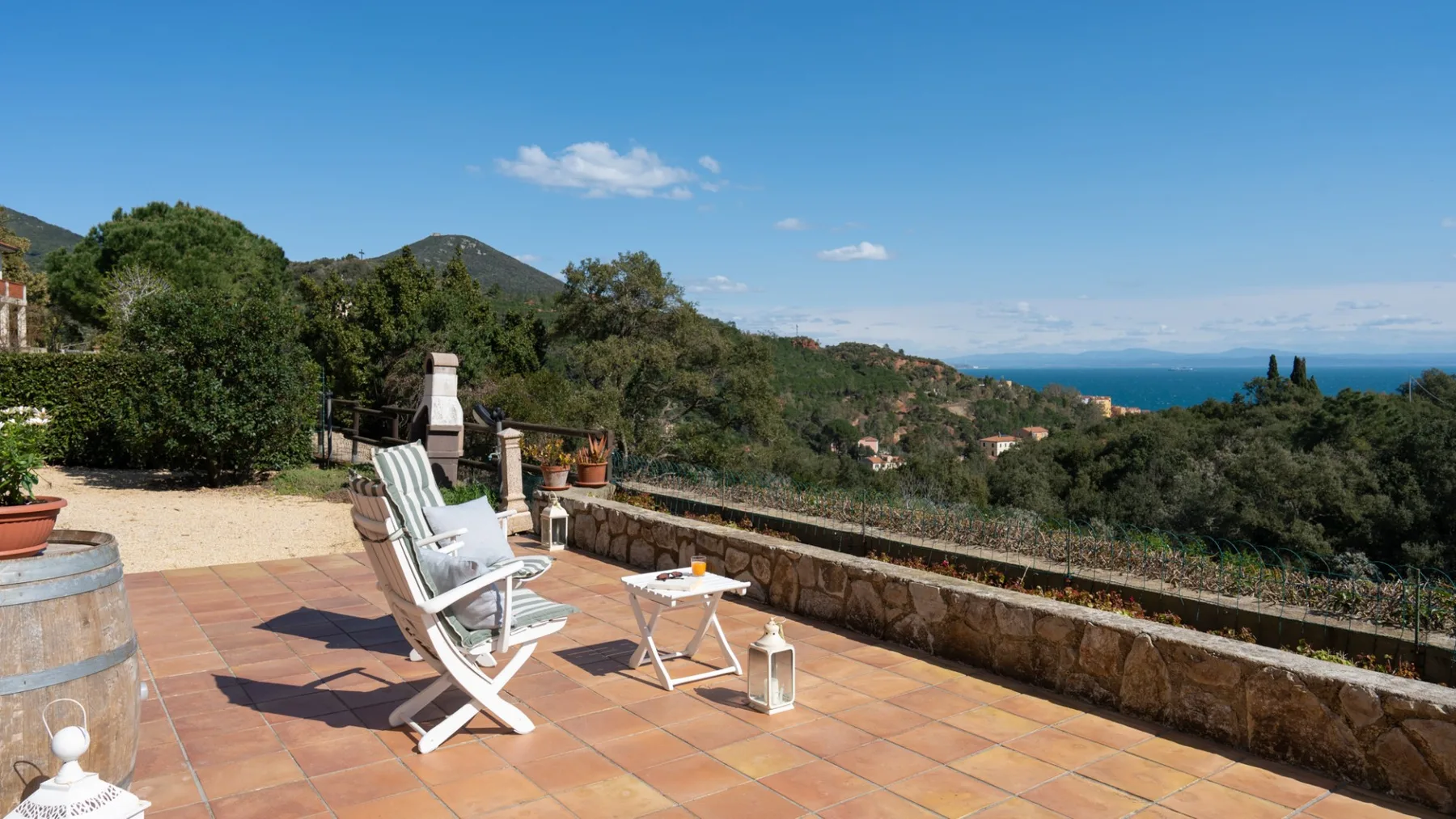 A sunny terrace with seating overlooks green hills and the sea.