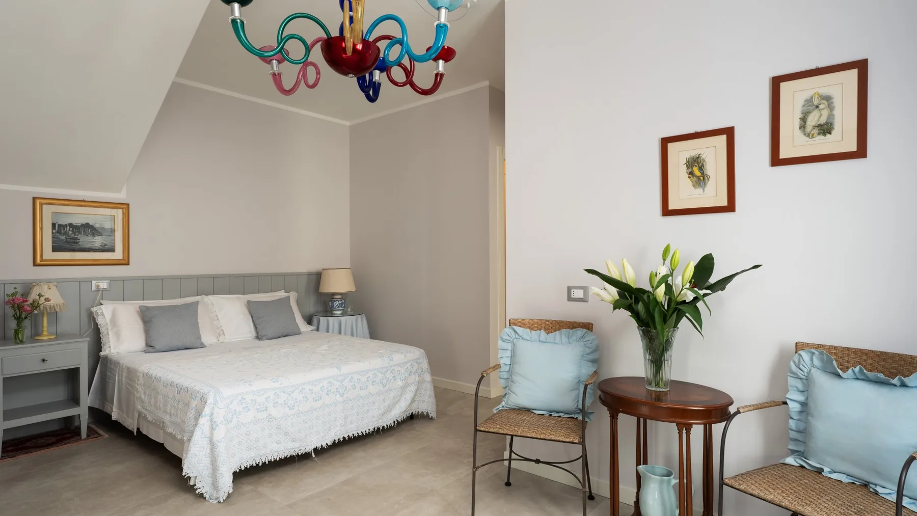 A bedroom with a bed and a colorful chandelier beneath the sloped ceiling.