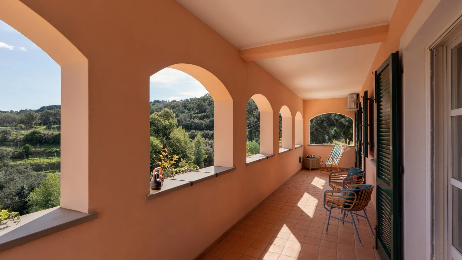 A covered terrace with arched openings overlooks a green landscape.
