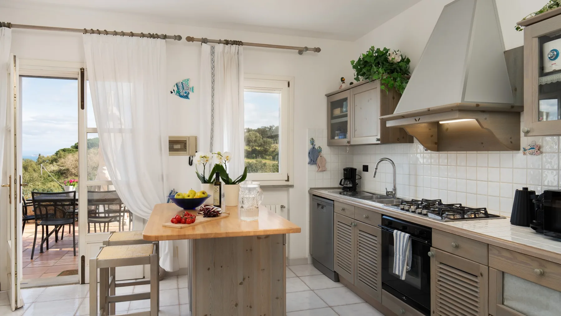 A bright kitchen with a wooden island and windows overlooking outdoor seating.