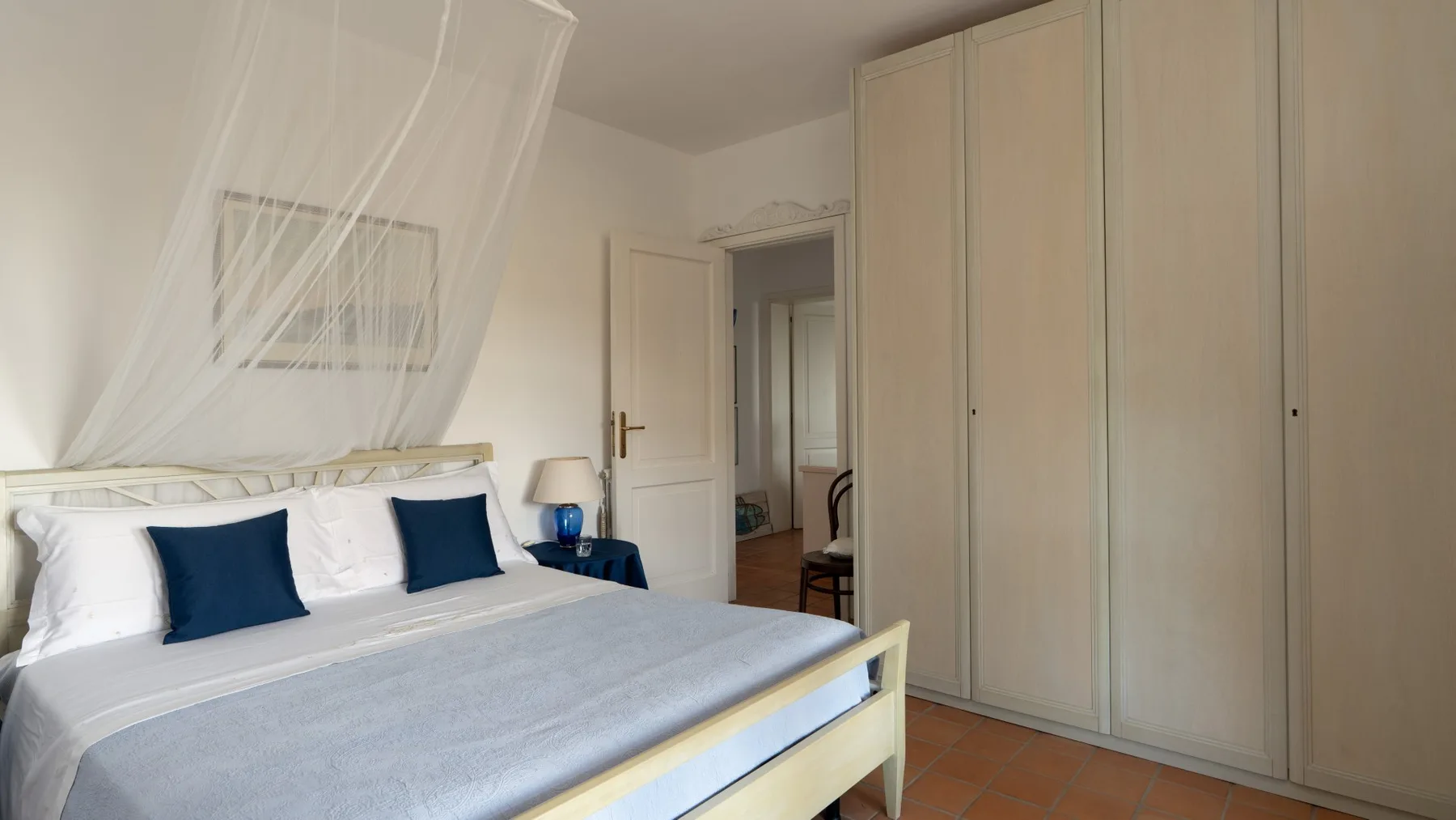 A bedroom with a double bed, sheer canopy curtains, and a tall wardrobe.