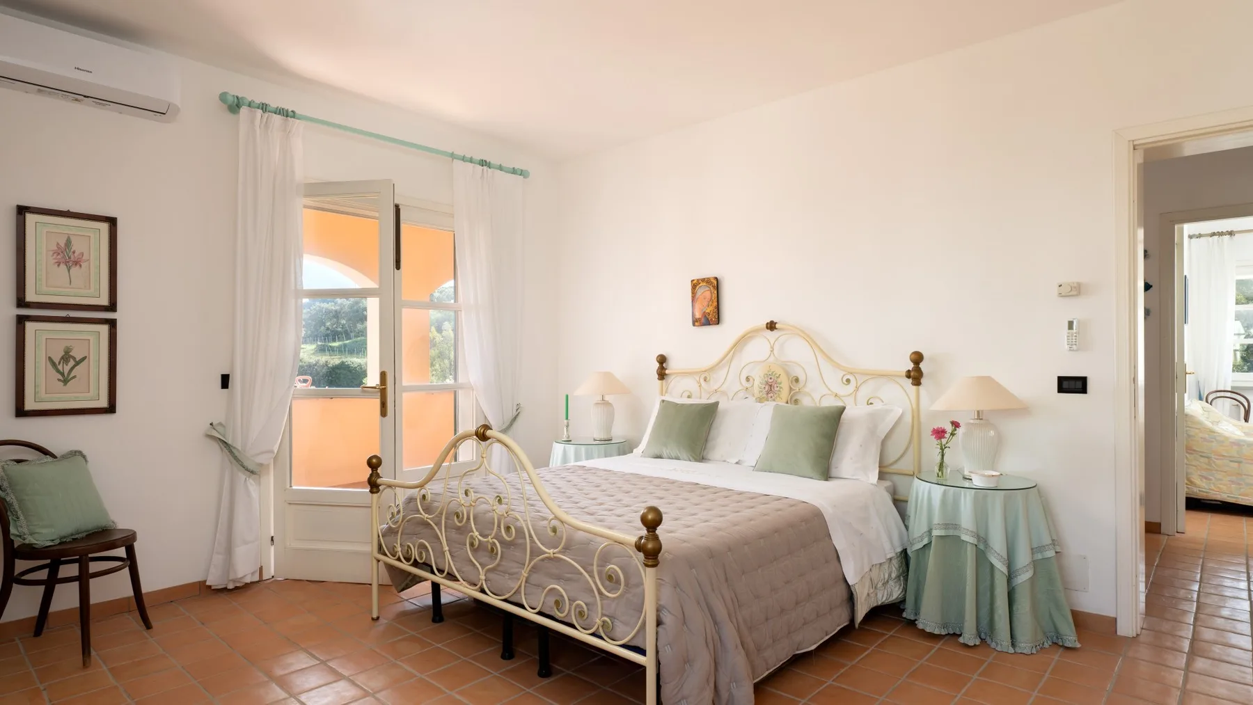 A bright bedroom with a large bed, bedside tables, and a glass door to a balcony.