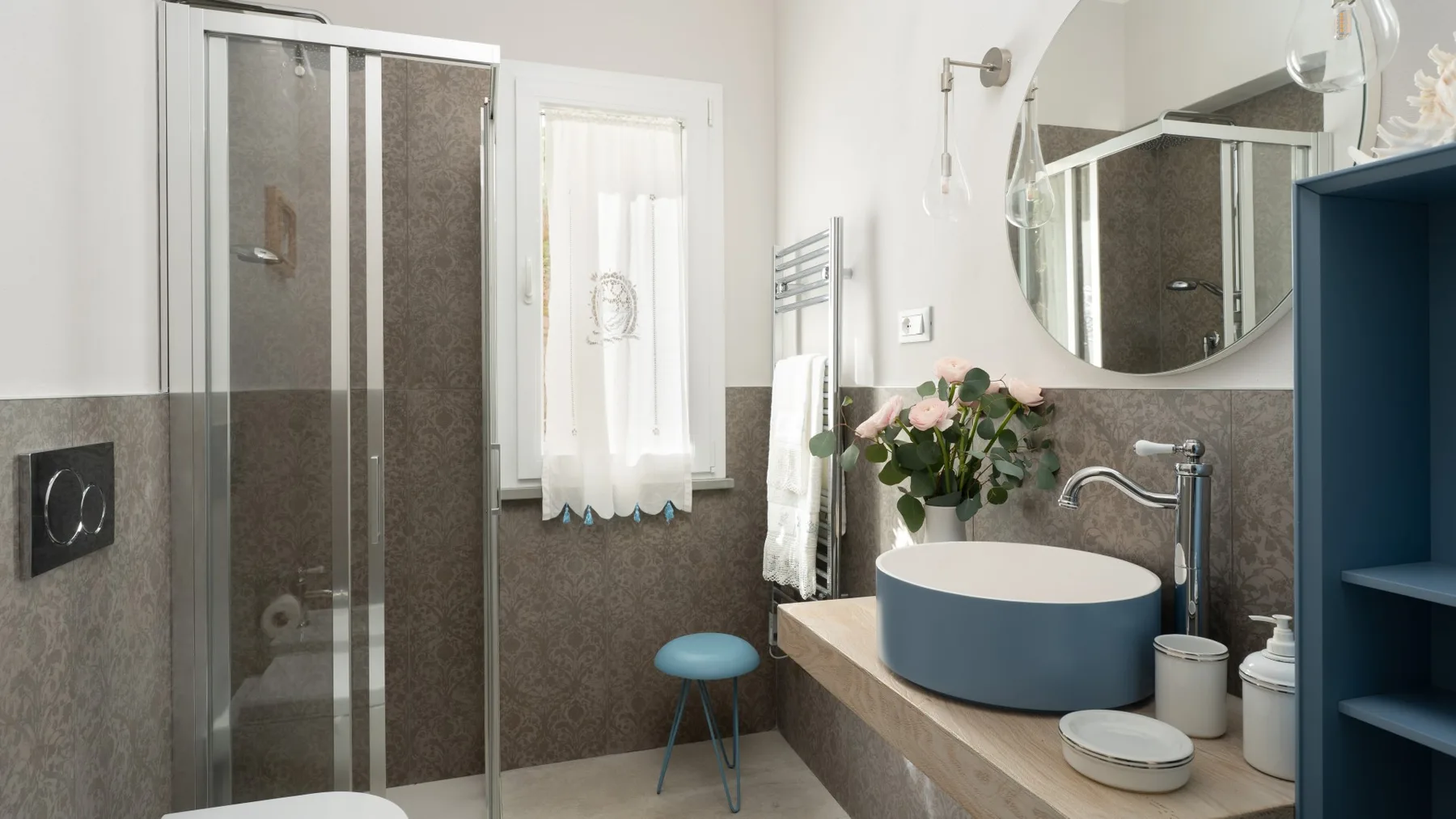 A bathroom with a glass shower, a round basin, and a window.
