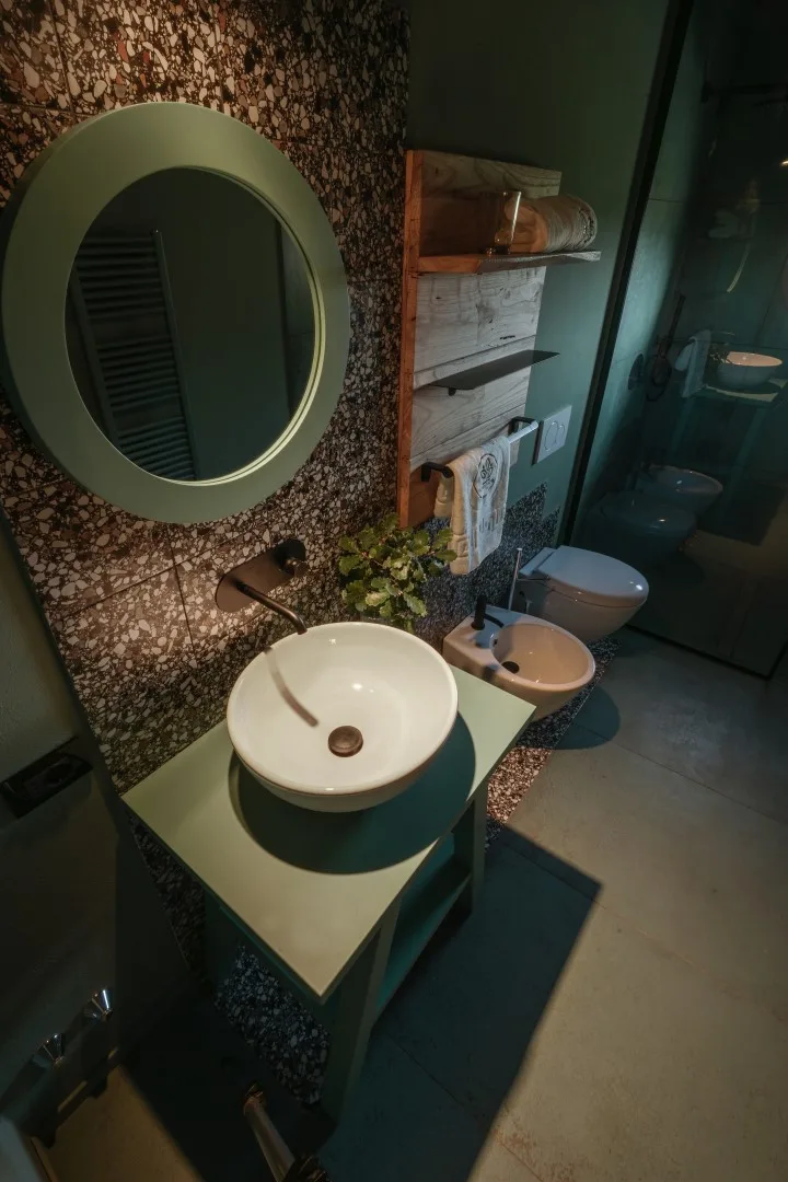 A bathroom vanity with a round mirror, vessel sink, and glass shower.