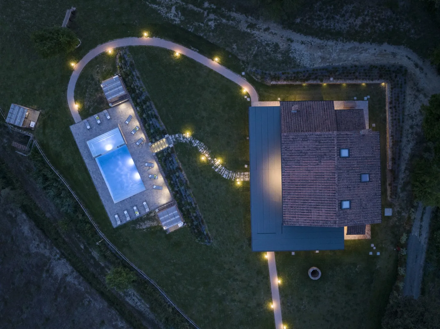 An aerial view shows a house beside a lit swimming pool and winding path.