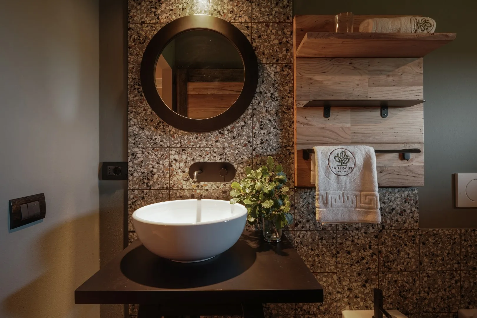A bathroom vanity with a round mirror, vessel sink, and wooden shelves.