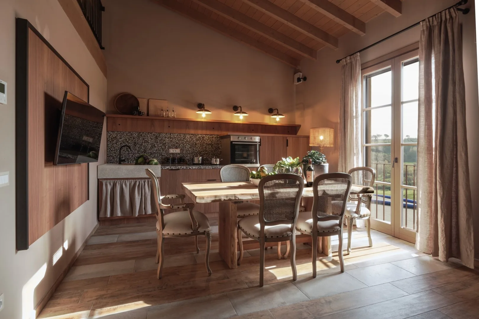 A dining area with a table and chairs beside a kitchen and tall glass doors.