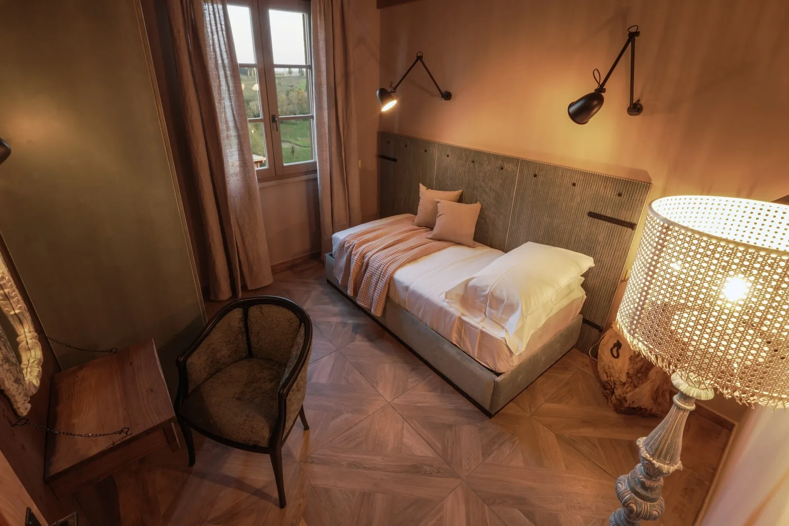 A bedroom with a bed, a window, and warm bedside lighting.