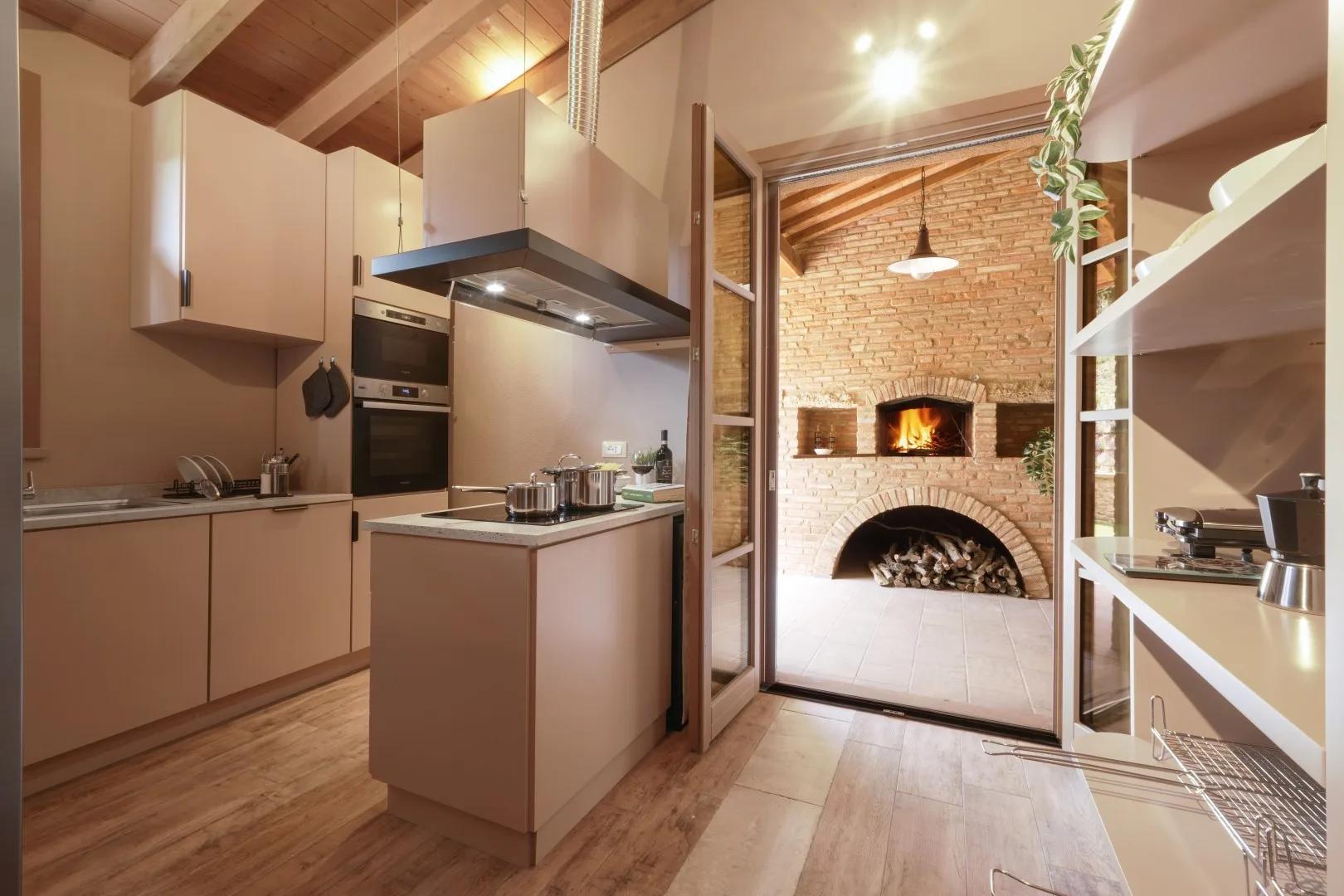 A modern kitchen opens onto a brick fireplace with a lit fire.