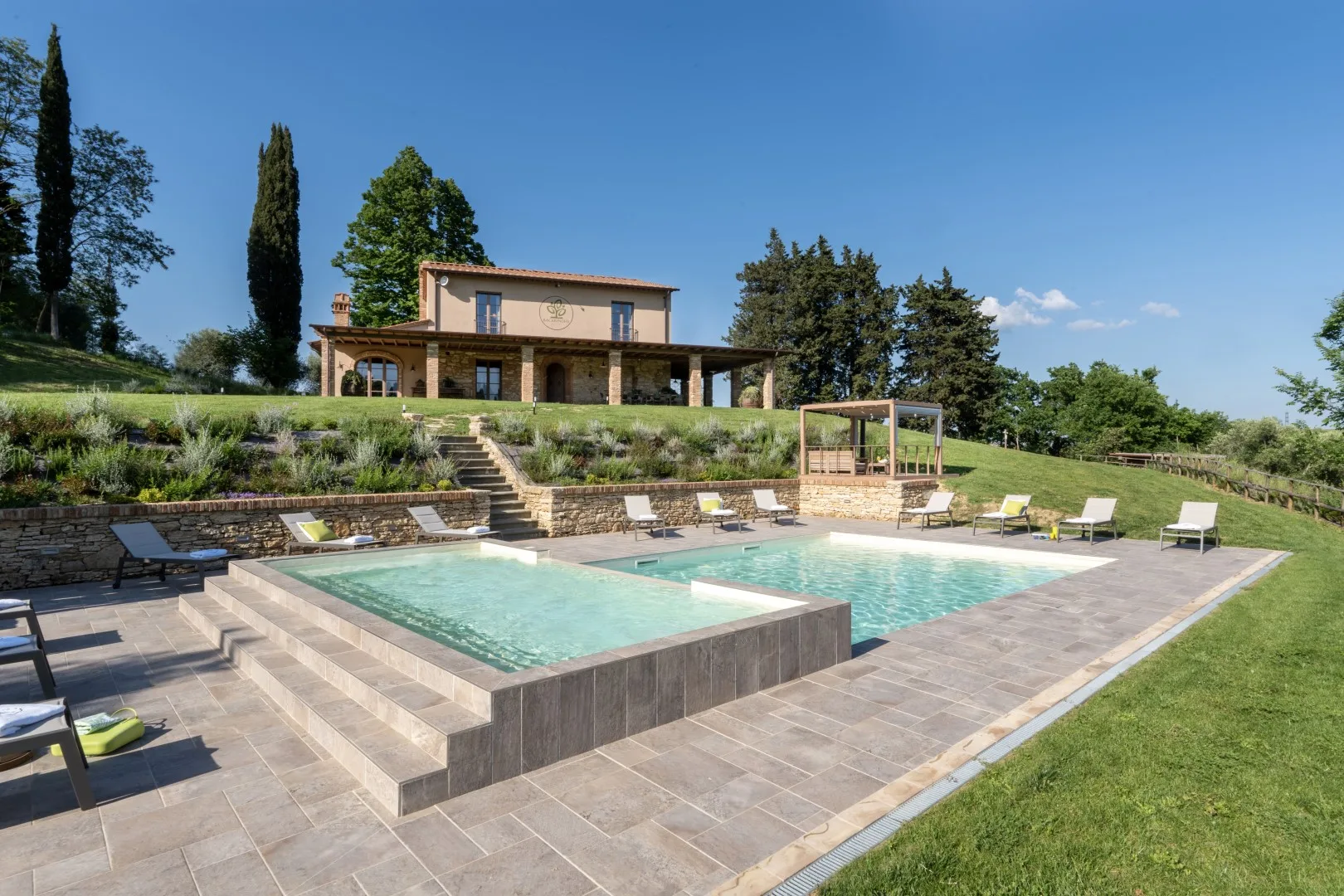 A swimming pool and sun loungers sit in a landscaped outdoor area below a villa.