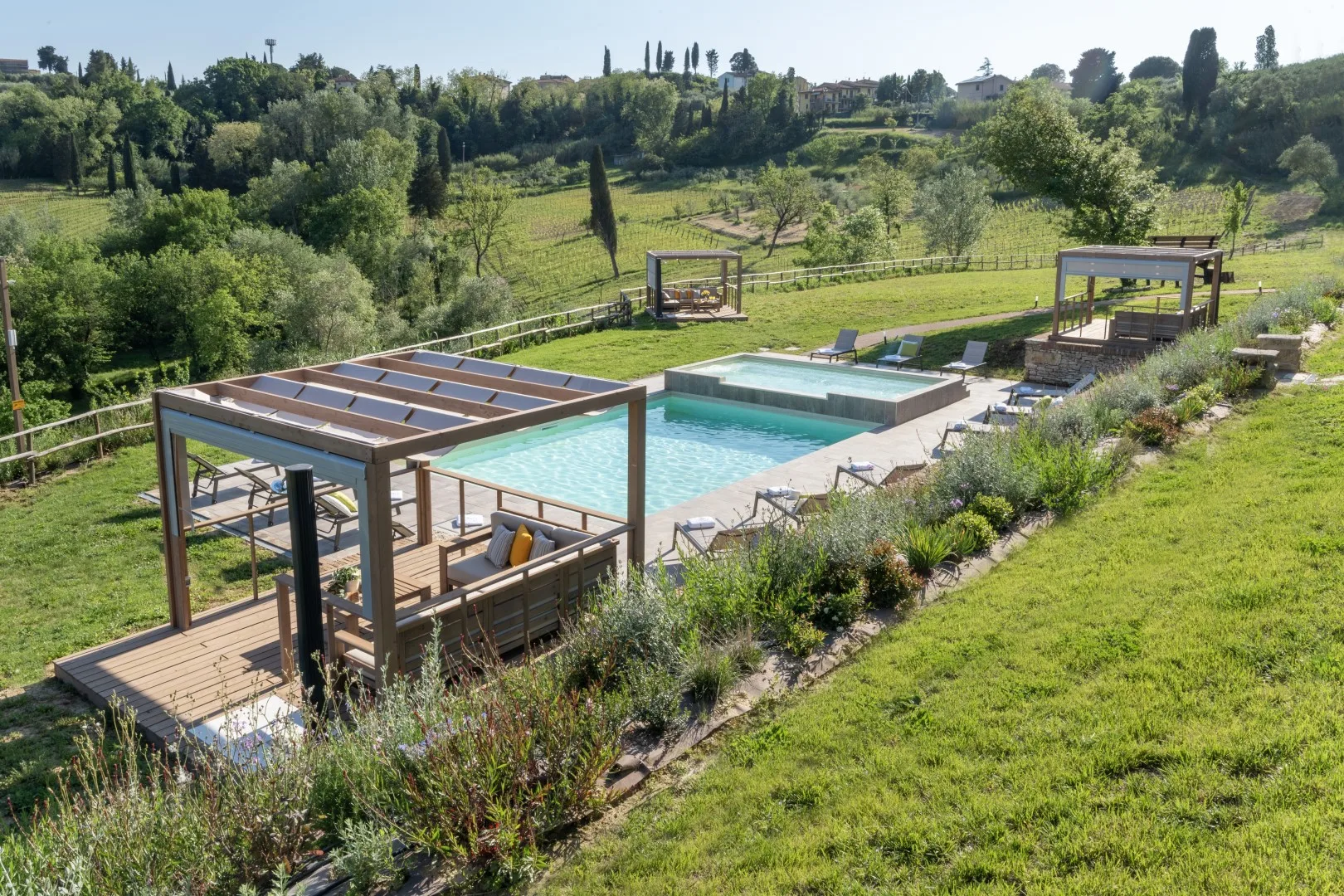 An outdoor swimming pool with a wooden pergola beside a green hillside.