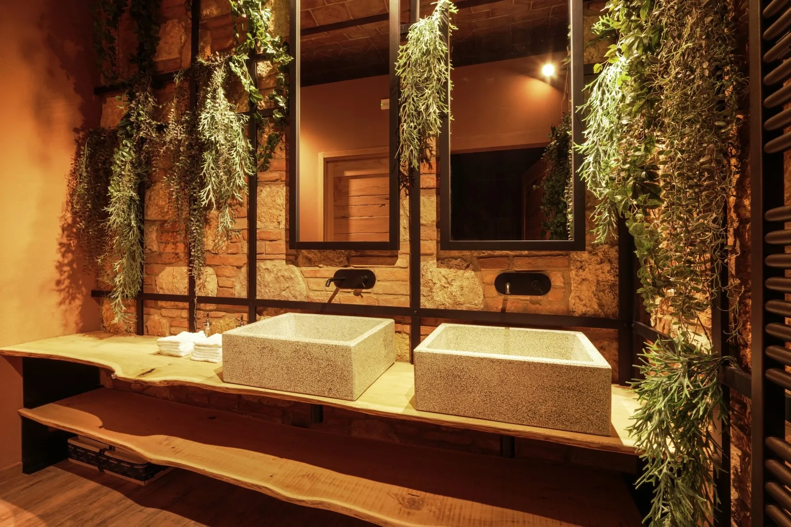 A warm-lit bathroom vanity with two rectangular sinks beneath mirrors and hanging plants.