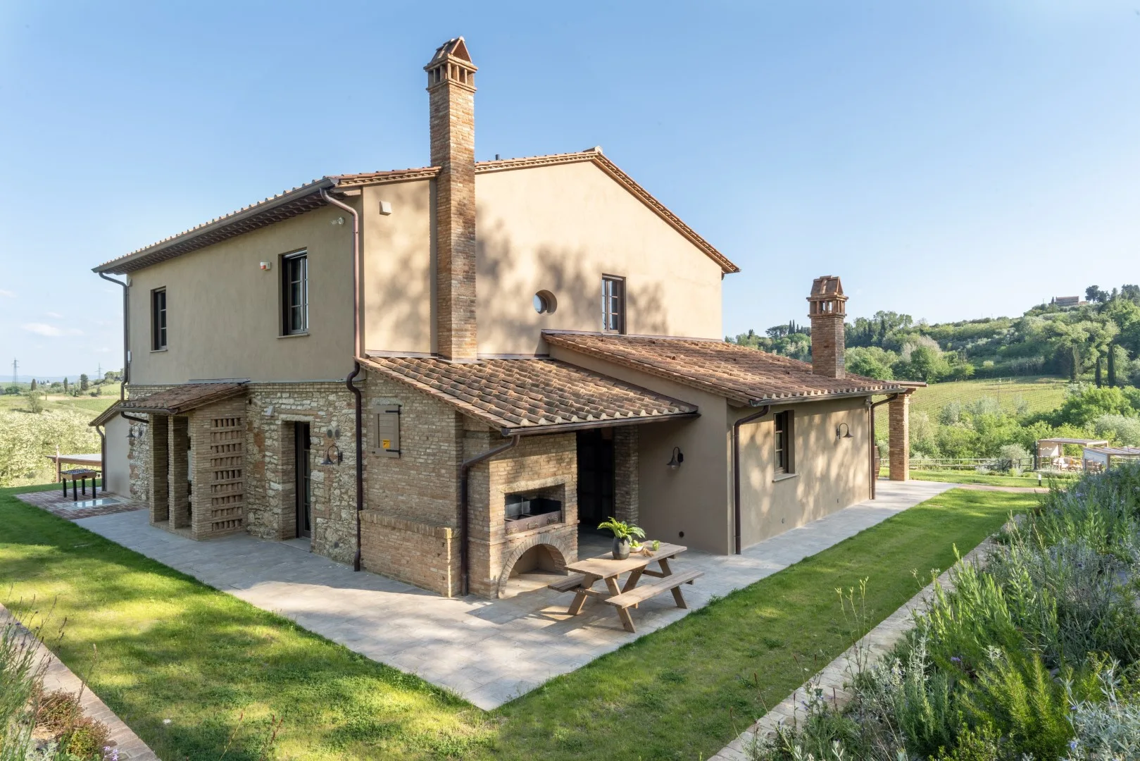 A countryside house with stone walls, tiled roofs, and a lawn.