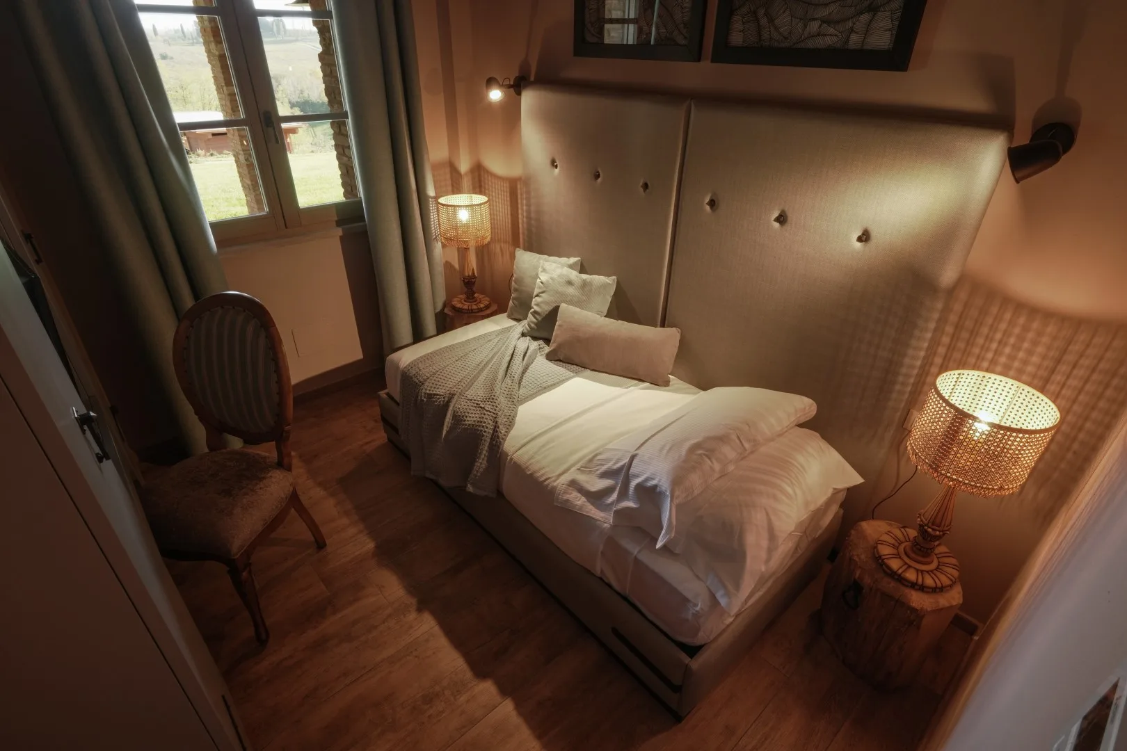 A warmly lit bedroom with a bed, bedside lamps, and a window.