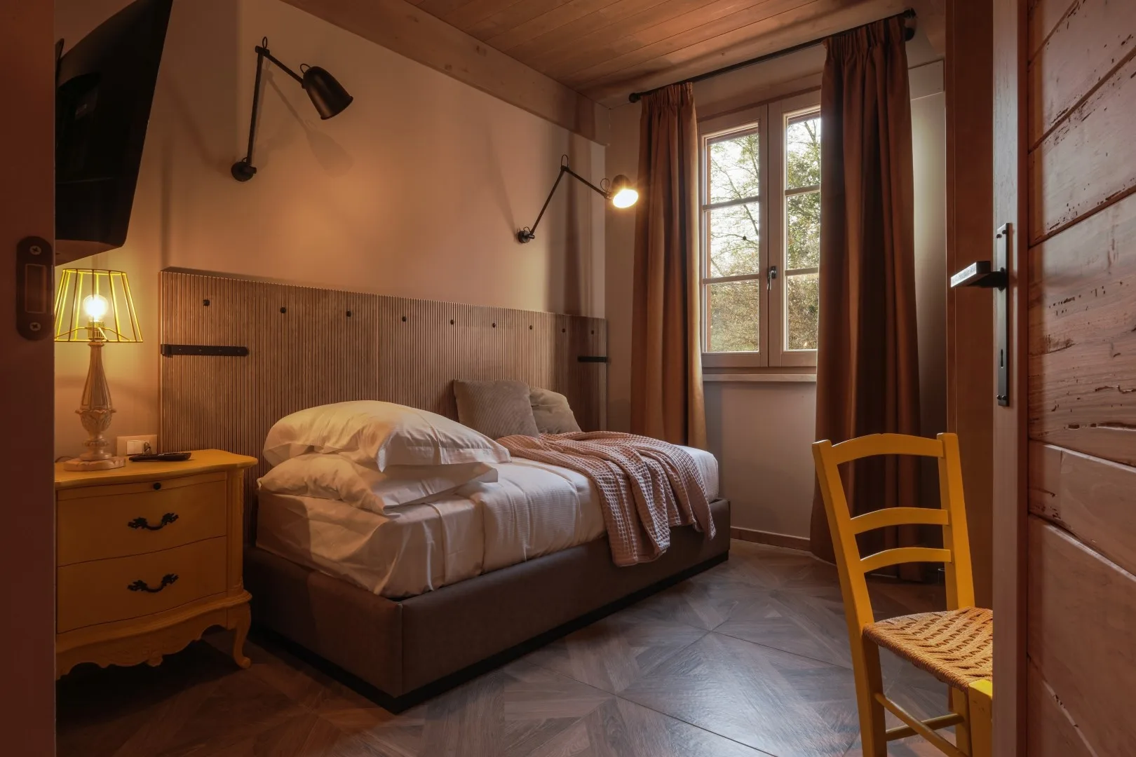 A bedroom with a neatly made bed beside a window.