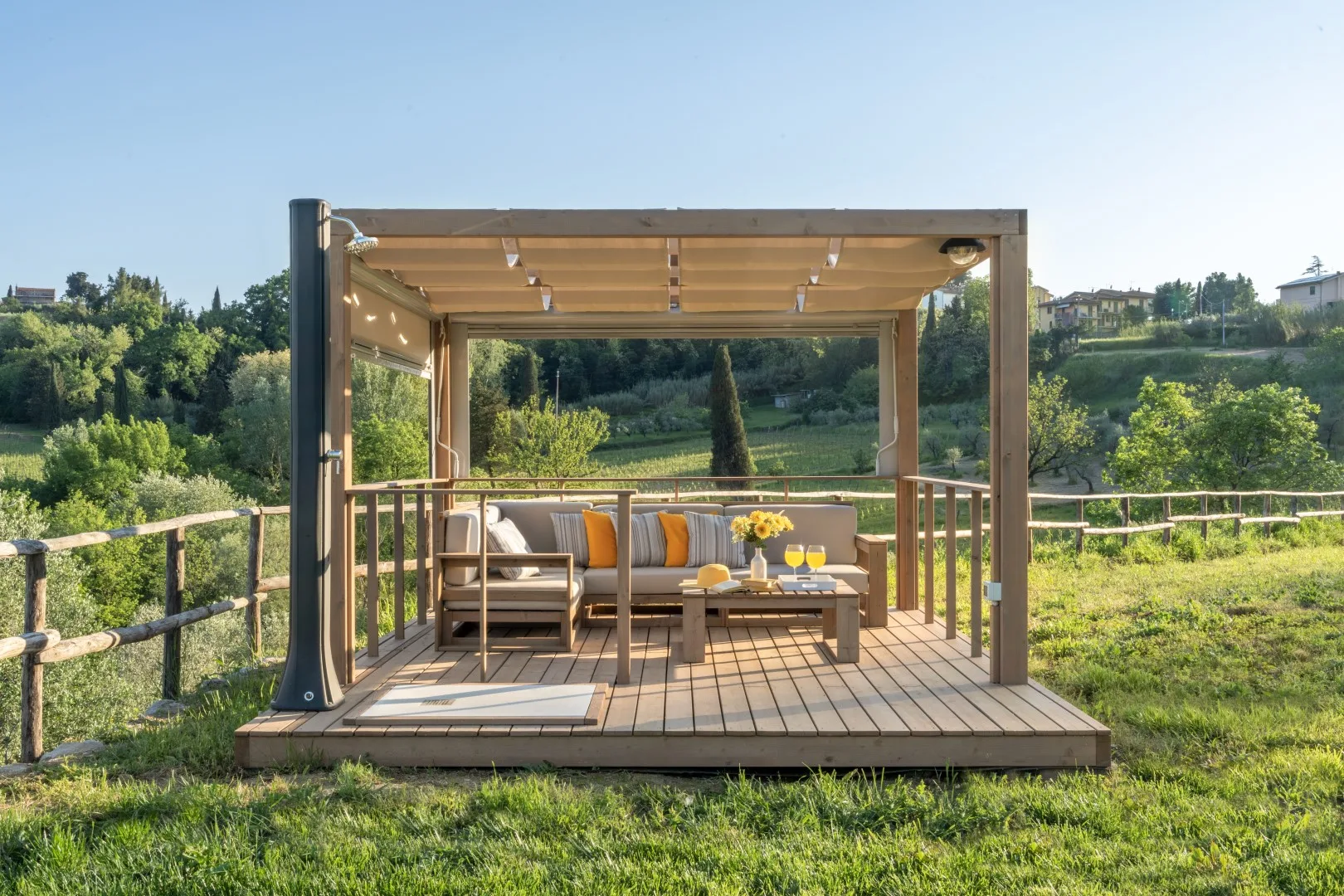A wooden pergola shelters an outdoor seating area overlooking a green landscape.