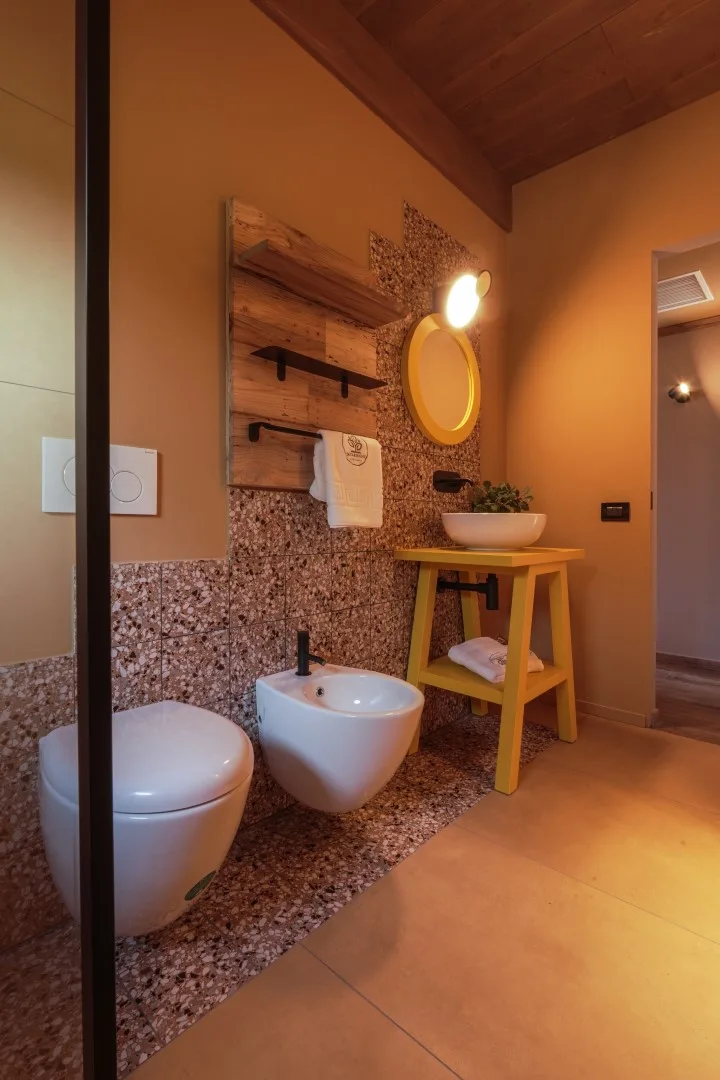 A warm-toned bathroom with a wall-mounted sink, toilet, and small wooden table.
