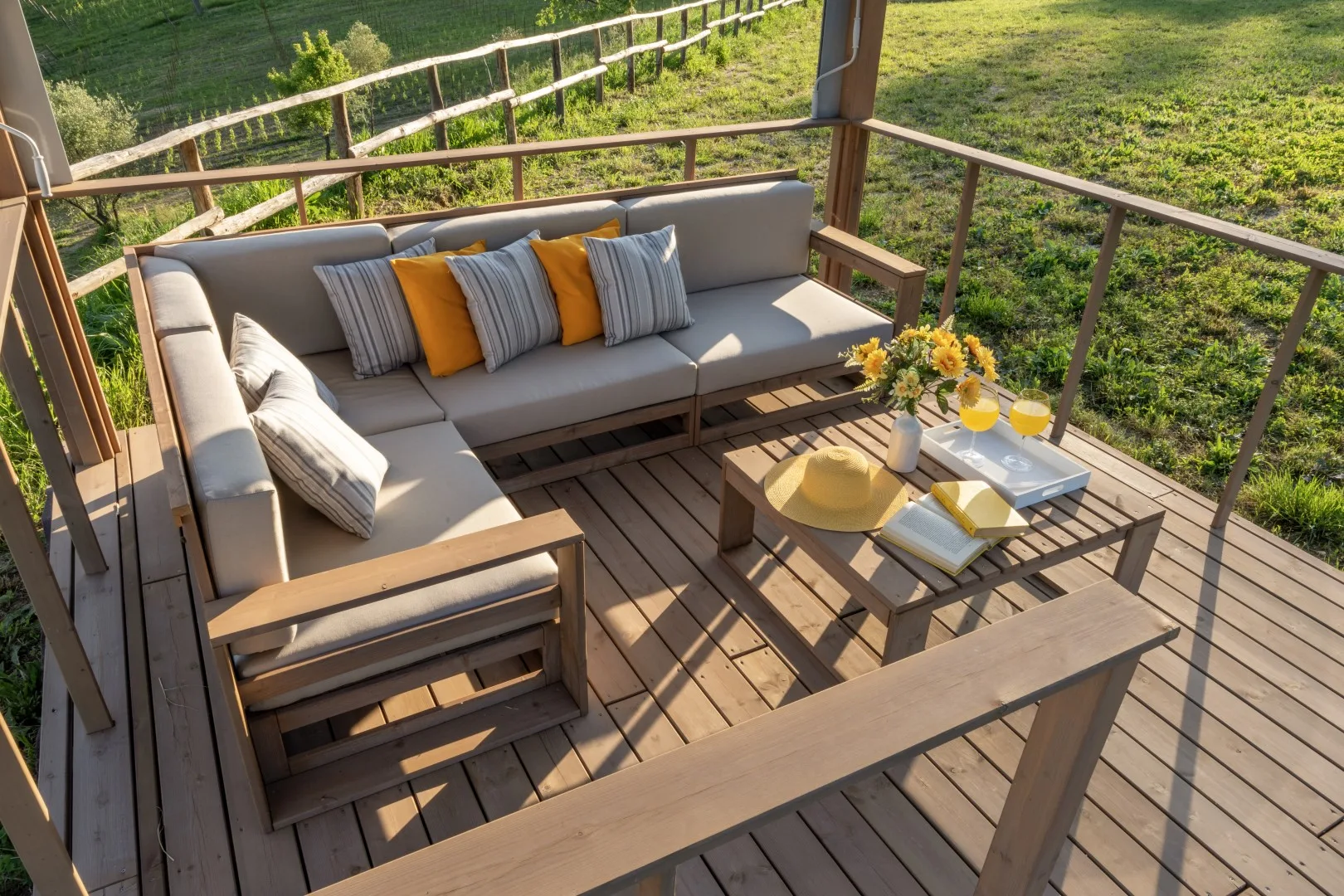 An outdoor seating area with cushioned furniture and a low table overlooks a grassy field.