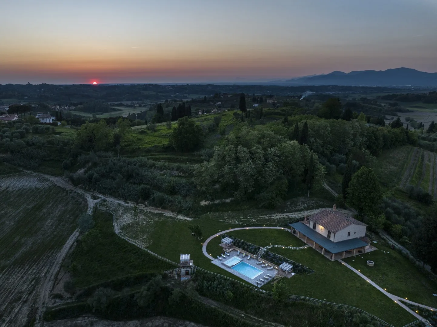 Aerial view of a countryside property with a house and swimming pool at sunset.