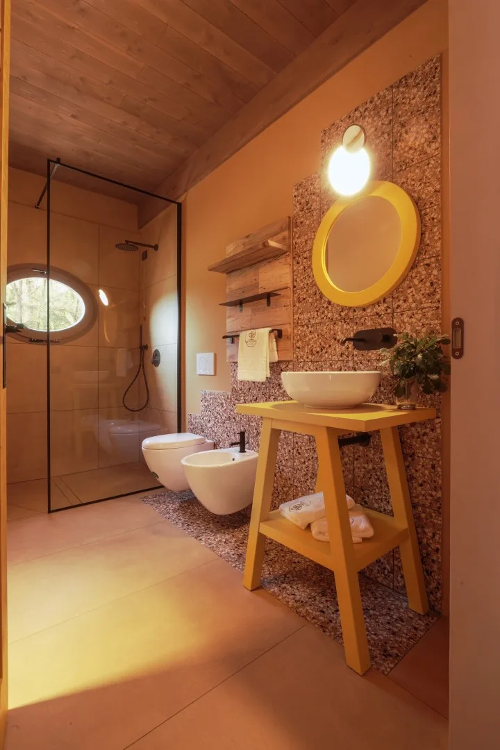 A warm-toned bathroom with a glass shower, sink, and round mirror.