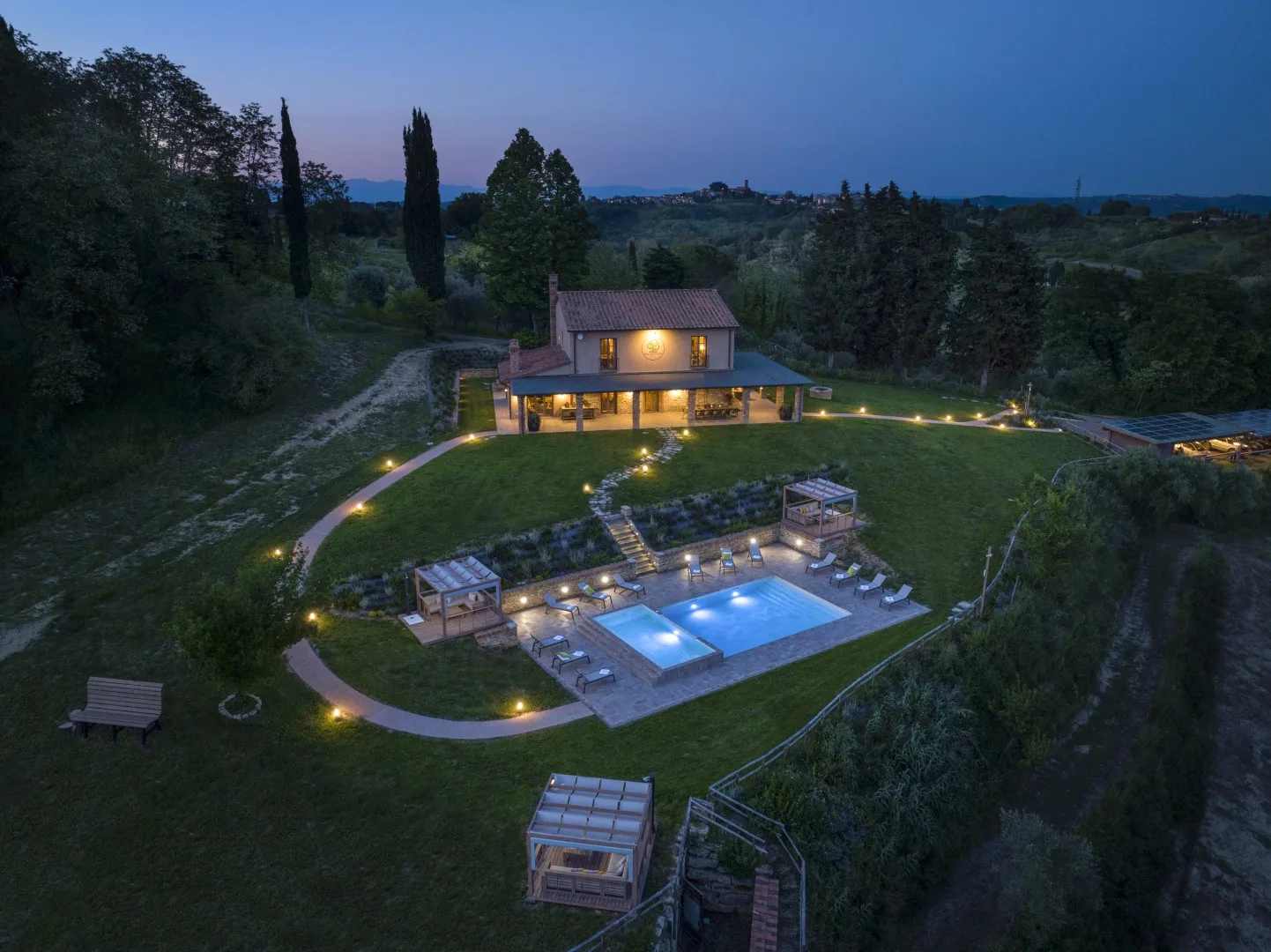 A landscaped property at dusk features a lit house, outdoor pool, and garden paths.
